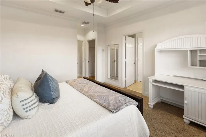 Bedroom featuring a tray ceiling, carpet floors, ornamental molding, a ceiling fan, and a desk