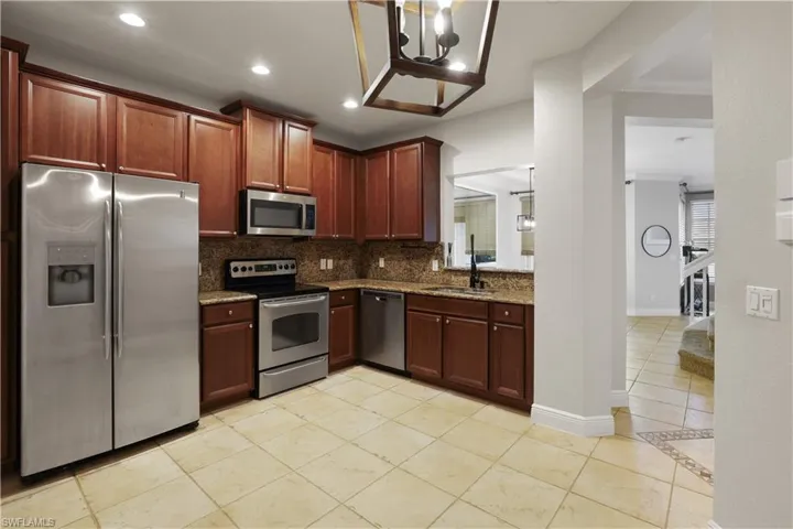 Kitchen with stainless steel appliances, dark stone counters, hanging light fixtures, a chandelier, and backsplash