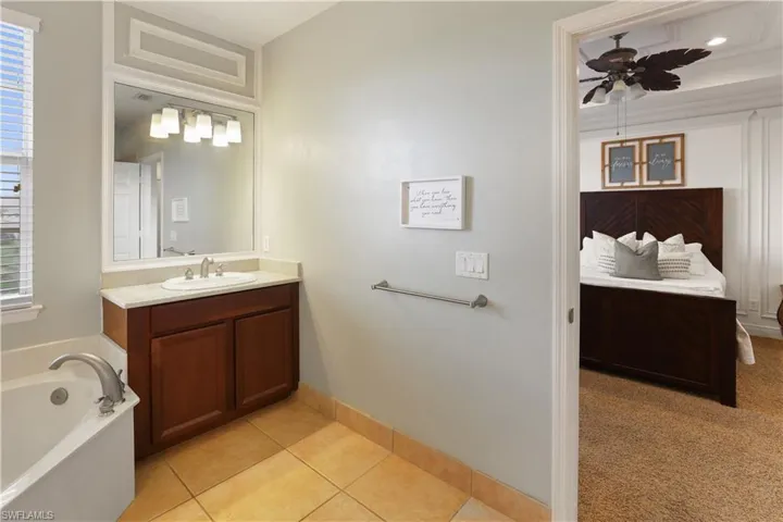 Bathroom featuring vanity, a bath, light colored carpet, light tile patterned floors, and ceiling fan