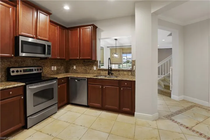 Kitchen featuring appliances with stainless steel finishes, dark stone countertops, light tile patterned floors, decorative backsplash, and inlaid floor details