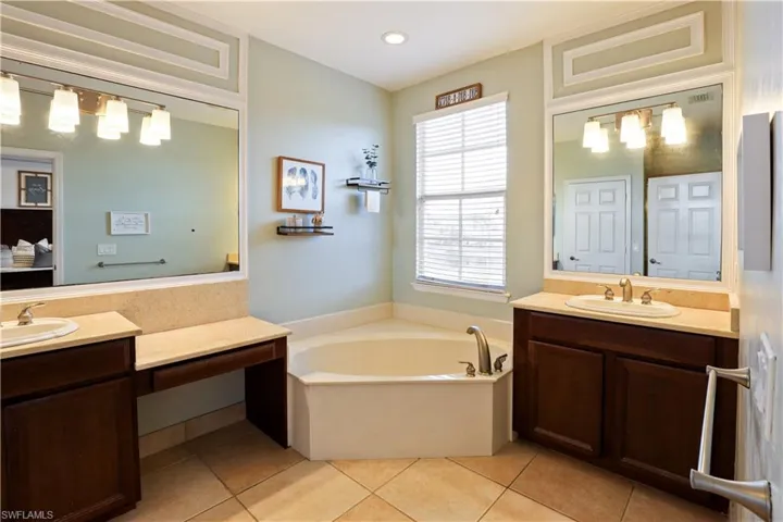 Full bath with two vanities, a bath, and light tile patterned floors