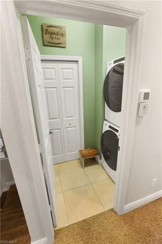 Laundry area with light carpet, light tile patterned floors, a textured wall, and stacked washer / dryer