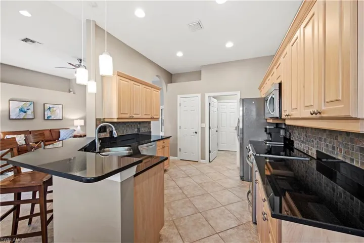 Kitchen featuring light brown cabinets, appliances with stainless steel finishes, backsplash, a breakfast bar, and light tile patterned floors