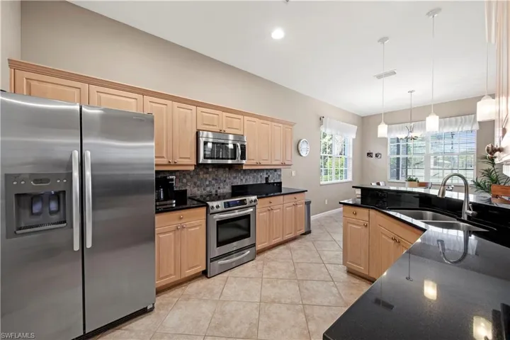 Kitchen with stainless steel appliances, light brown cabinetry, pendant lighting, light tile patterned flooring, and dark stone countertops