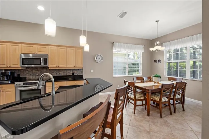 Kitchen with a breakfast bar, light tile patterned floors, appliances with stainless steel finishes, backsplash, and decorative light fixtures
