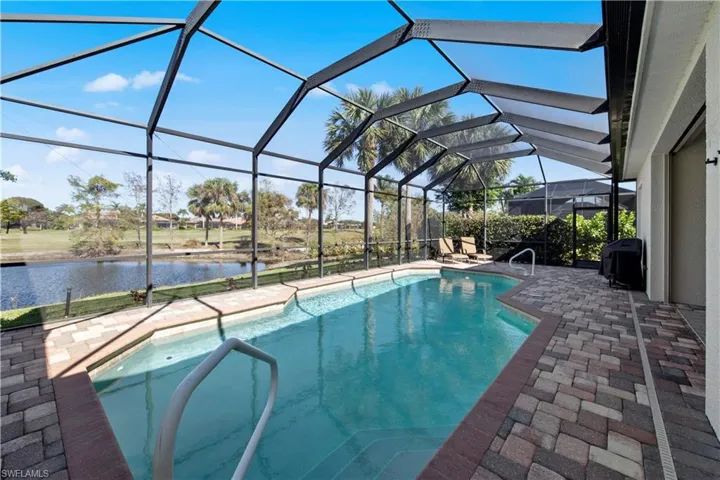 Outdoor pool with a sunroom, a patio, glass enclosure, a grill, and a water view