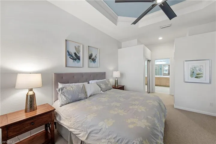 Bedroom with light colored carpet, ensuite bathroom, a tray ceiling, a ceiling fan, and recessed lighting