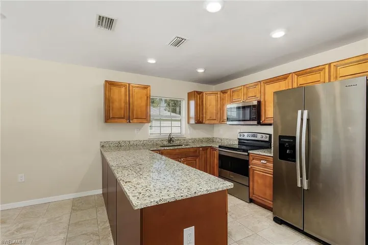 Kitchen with stainless steel appliances, a peninsula, light stone countertops, brown cabinetry, and recessed lighting