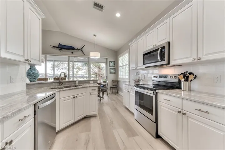 Kitchen featuring white cabinets, lofted ceiling, stainless steel appliances, sink, and hanging light fixtures