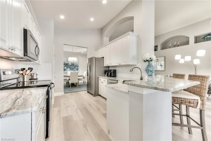 Kitchen with kitchen peninsula, appliances with stainless steel finishes, a kitchen breakfast bar, light stone countertops, and white cabinets