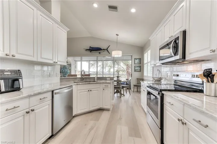 Kitchen featuring white cabinets, decorative light fixtures, stainless steel appliances, sink, and vaulted ceiling