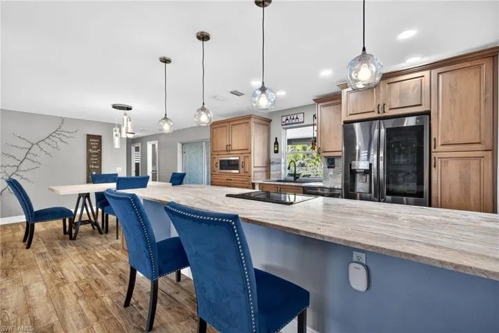 Kitchen with pendant lighting, a kitchen breakfast bar, light stone counters, black appliances, and light wood finished floors