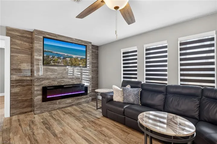 Living area with wood finished floors, ceiling fan, and a large fireplace