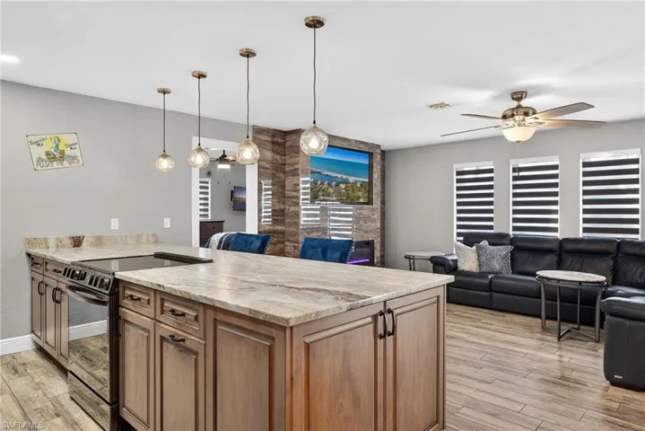 Kitchen featuring black electric range oven, light stone counters, pendant lighting, light wood-style floors, and a peninsula