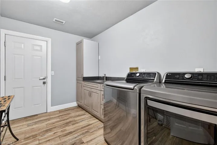 Laundry area with washing machine and dryer, light wood-type flooring, and cabinet space