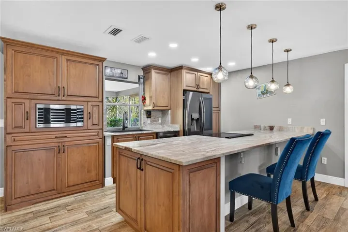 Kitchen with a kitchen breakfast bar, a peninsula, stainless steel appliances, decorative light fixtures, and brown cabinetry