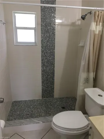 Bathroom with curtained shower, tile patterned floors, vanity, and toilet