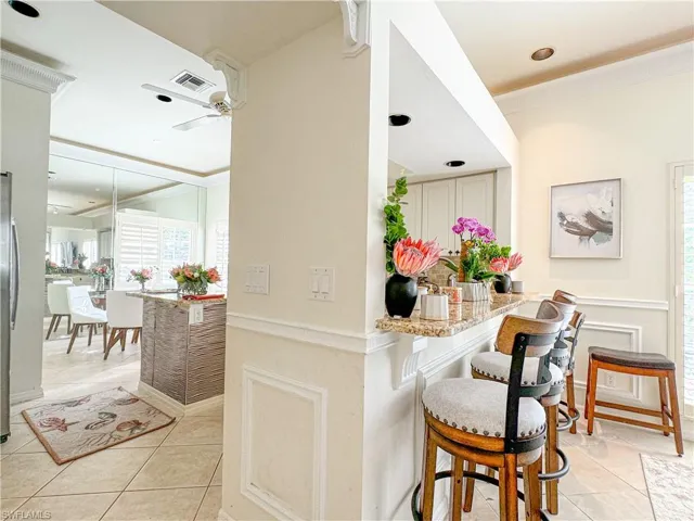Kitchen featuring light tile floors, light stone counters, ceiling fan, and a breakfast bar