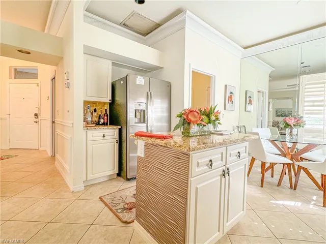 Kitchen with light stone counters, stainless steel fridge with ice dispenser, light tile floors, and tasteful backsplash