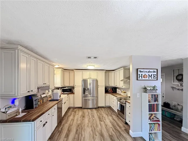 Kitchen with light wood finished floors, stainless steel appliances, a textured ceiling, butcher block counters, and cream cabinets