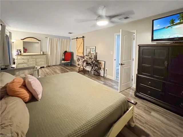 Bedroom featuring light wood finished floors, a barn door, and ceiling fan