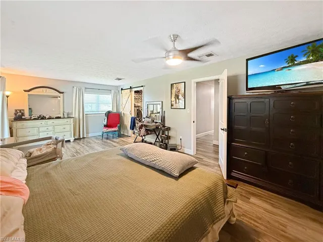 Bedroom with light wood-style floors, a barn door, ceiling fan, and a textured ceiling