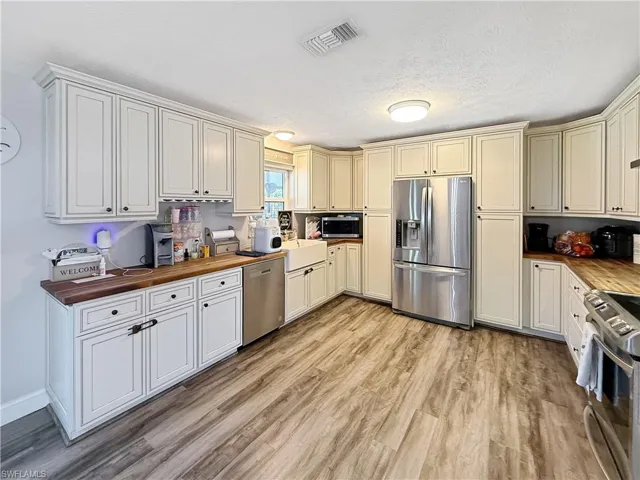 Kitchen with wooden counters, stainless steel appliances, cream cabinetry, light wood finished floors, and a textured ceiling