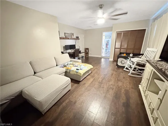 Living area featuring dark wood-style flooring, ceiling fan, and a desk