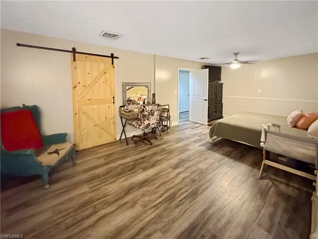 Bedroom with a barn door, wood finished floors, and ceiling fan