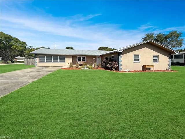 Ranch-style house featuring stucco siding, a front yard, concrete driveway, and a metal roof