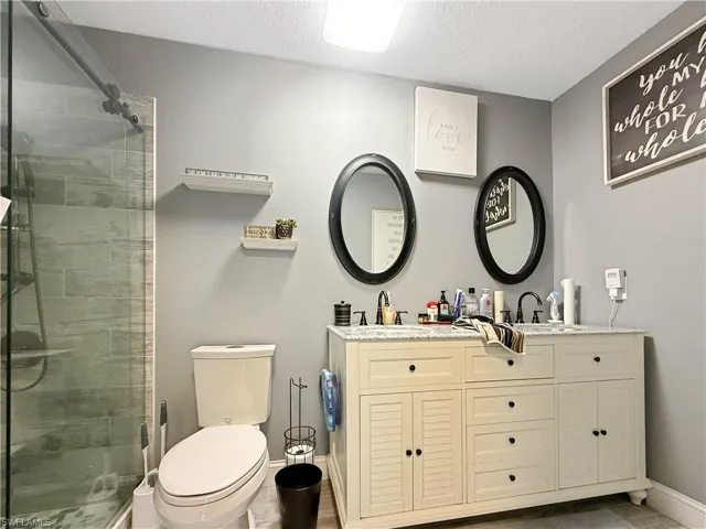 Bathroom with a textured ceiling, double vanity, and a shower stall
