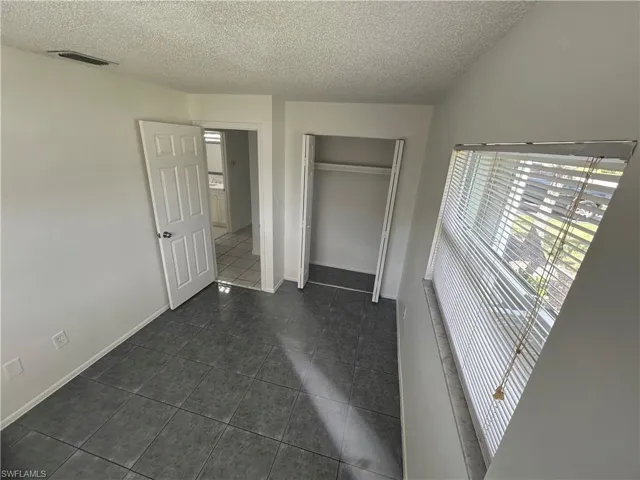 Unfurnished bedroom with a closet, a textured ceiling, and dark tile patterned floors