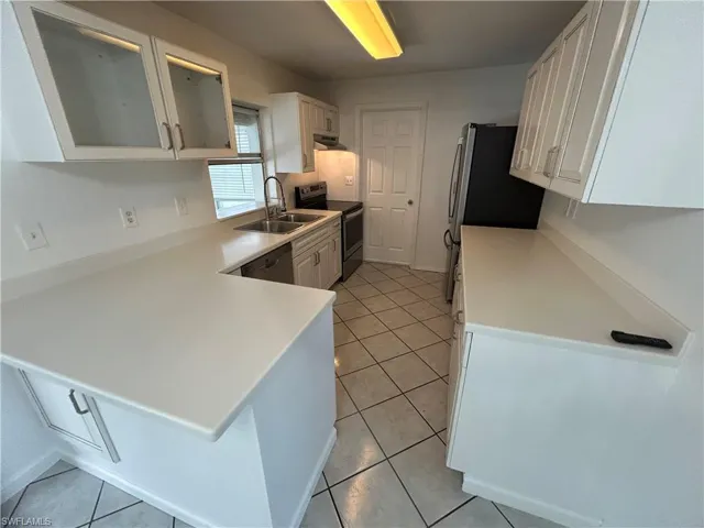 Kitchen with kitchen peninsula, white cabinetry, stainless steel appliances, and sink