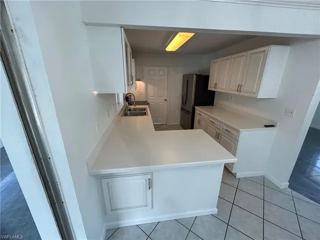 Kitchen featuring sink, light tile patterned flooring, kitchen peninsula, and stainless steel refrigerator