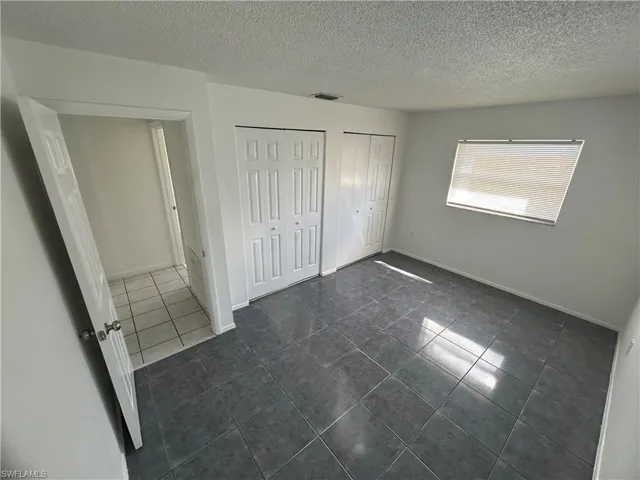 Unfurnished bedroom with dark tile patterned flooring, multiple closets, and a textured ceiling