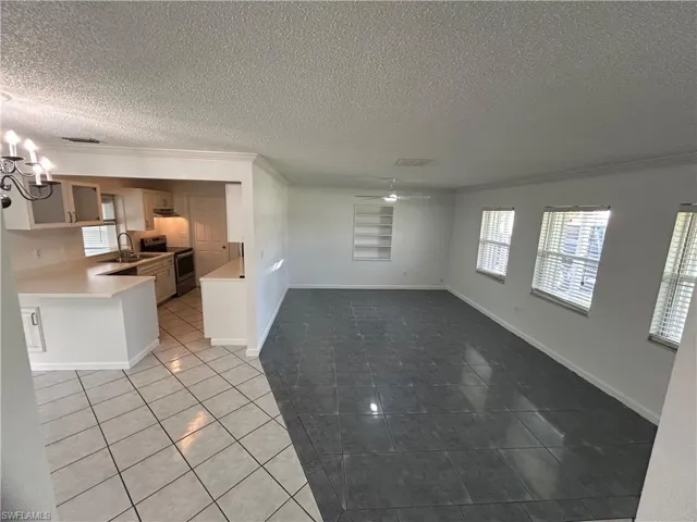 Kitchen featuring ceiling fan with notable chandelier, a textured ceiling, stainless steel electric range oven, crown molding, and light tile patterned floors