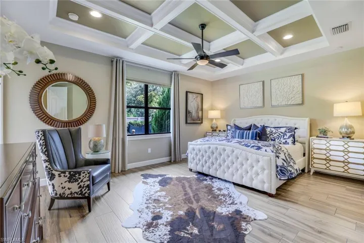 Owner's suite featuring coffered ceiling with extensive beam woodwork, ceiling fan, wood-like plank floor tile