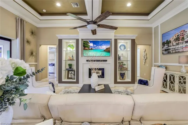 Large tiled great room featuring 14' coffered ornamental ceiling with crown molding, a decorative fireplace, and ceiling fan