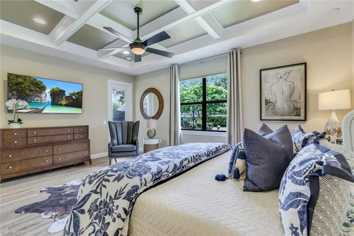 Spacious owner's suite featuring door leading to backyard, coffered beamed ceiling, and wood-like plank tile flooring