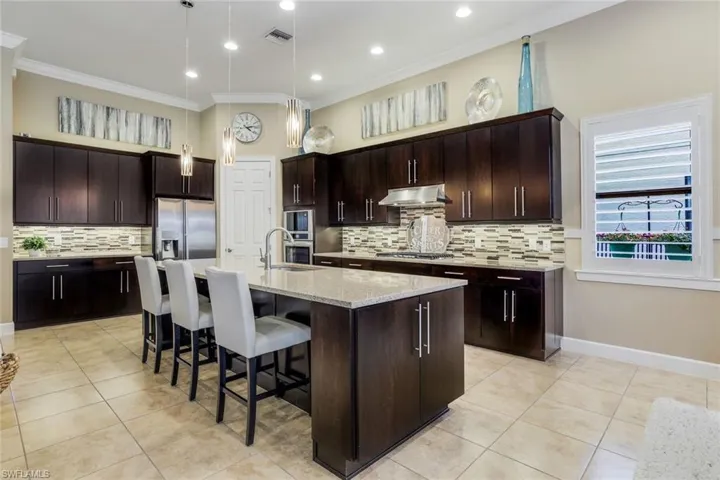 Custom, natural gas, highly upgraded gourmet kitchen with solid surface countertops, a large island with sink, stainless steel appliances, pendant lighting, and tiled backsplash