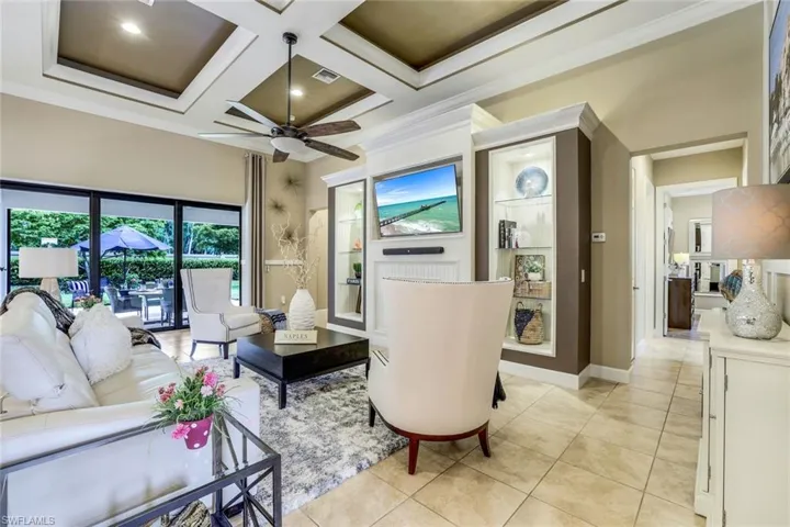 Tiled living room with coffered ceiling, ceiling fan, beam ceiling, large custom built-in wall unit and ornamental molding