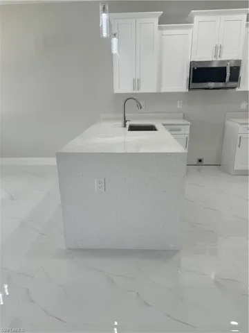 Kitchen featuring light tile patterned flooring, kitchen peninsula, light stone counters, pendant lighting, and sink
