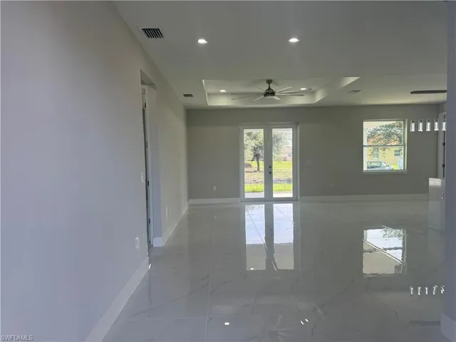 Empty room featuring light tile patterned flooring, french doors, ceiling fan, and a raised ceiling