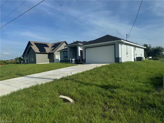 View of front of property with a garage, a front lawn, solar panels, and central AC unit