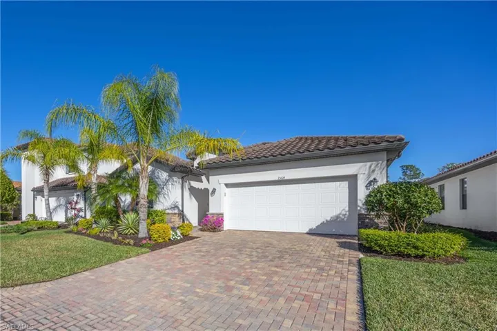 View of front of home with a front lawn, stucco siding, decorative driveway, a tiled roof, and an attached garage