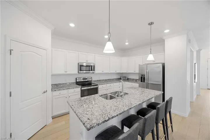Kitchen with a kitchen bar, stainless steel appliances, light wood finished floors, light stone countertops, and white cabinets
