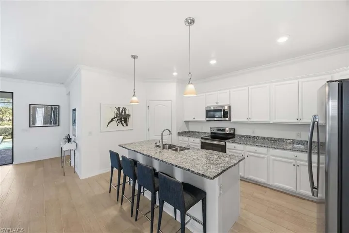 Kitchen with stainless steel appliances, white cabinets, light stone countertops, a kitchen bar, and crown molding