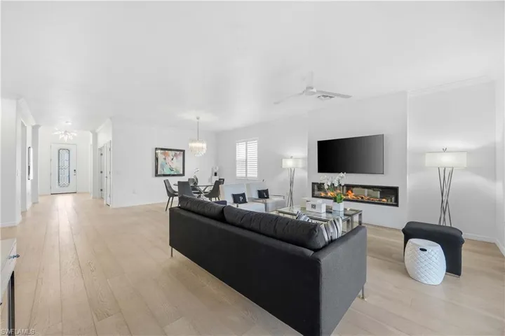 Living area with ornamental molding, a ceiling fan, light wood-type flooring, a glass covered fireplace, and a chandelier