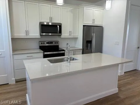 Kitchen with appliances with stainless steel finishes, hardwood / wood-style floors, sink, an island with sink, and white cabinets