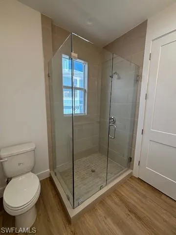 Bathroom featuring hardwood / wood-style flooring, toilet, and a shower with door